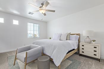 A bedroom with a bed, chair, and ceiling fan.